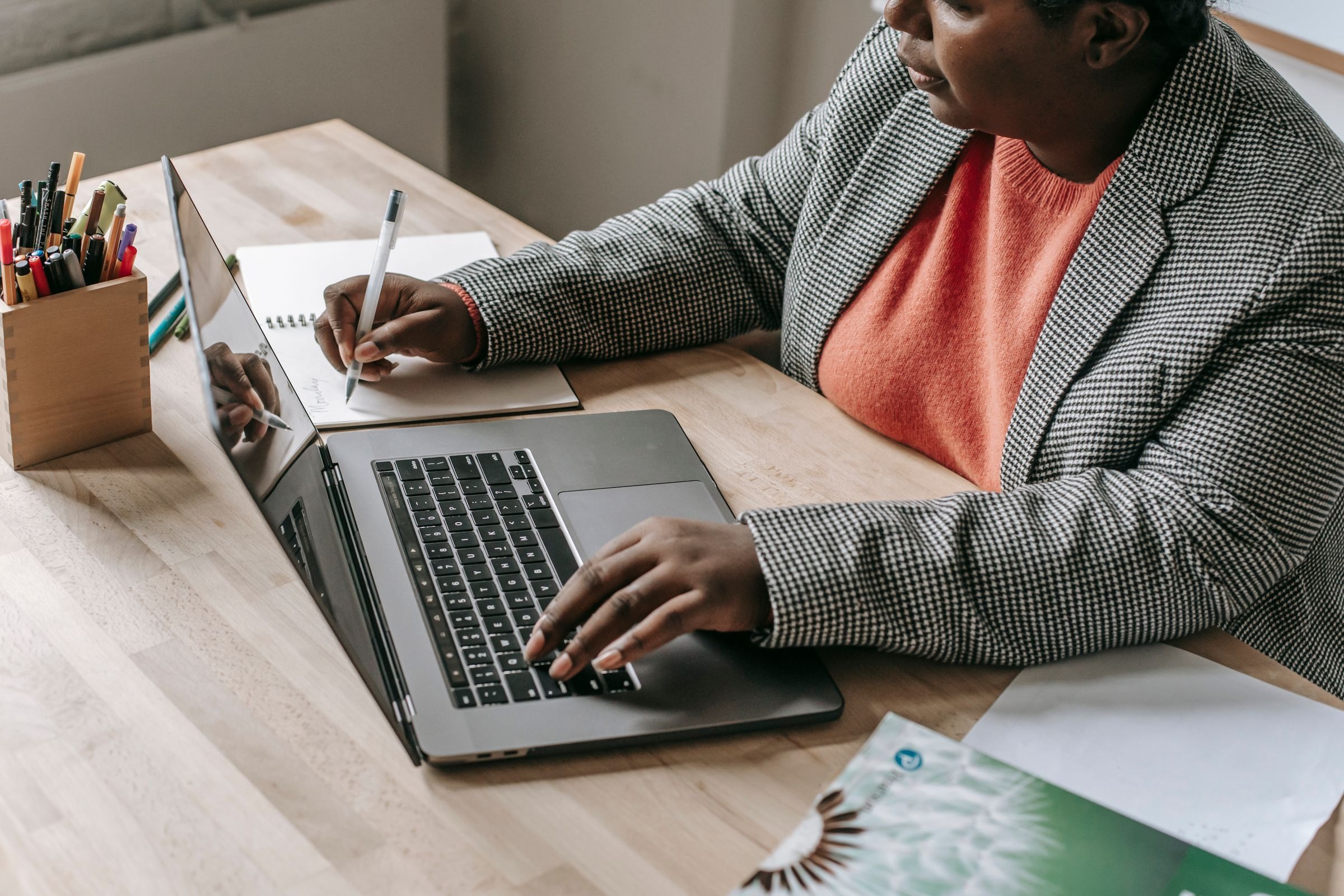 Black woman working on laptop and taking notes at an office desk