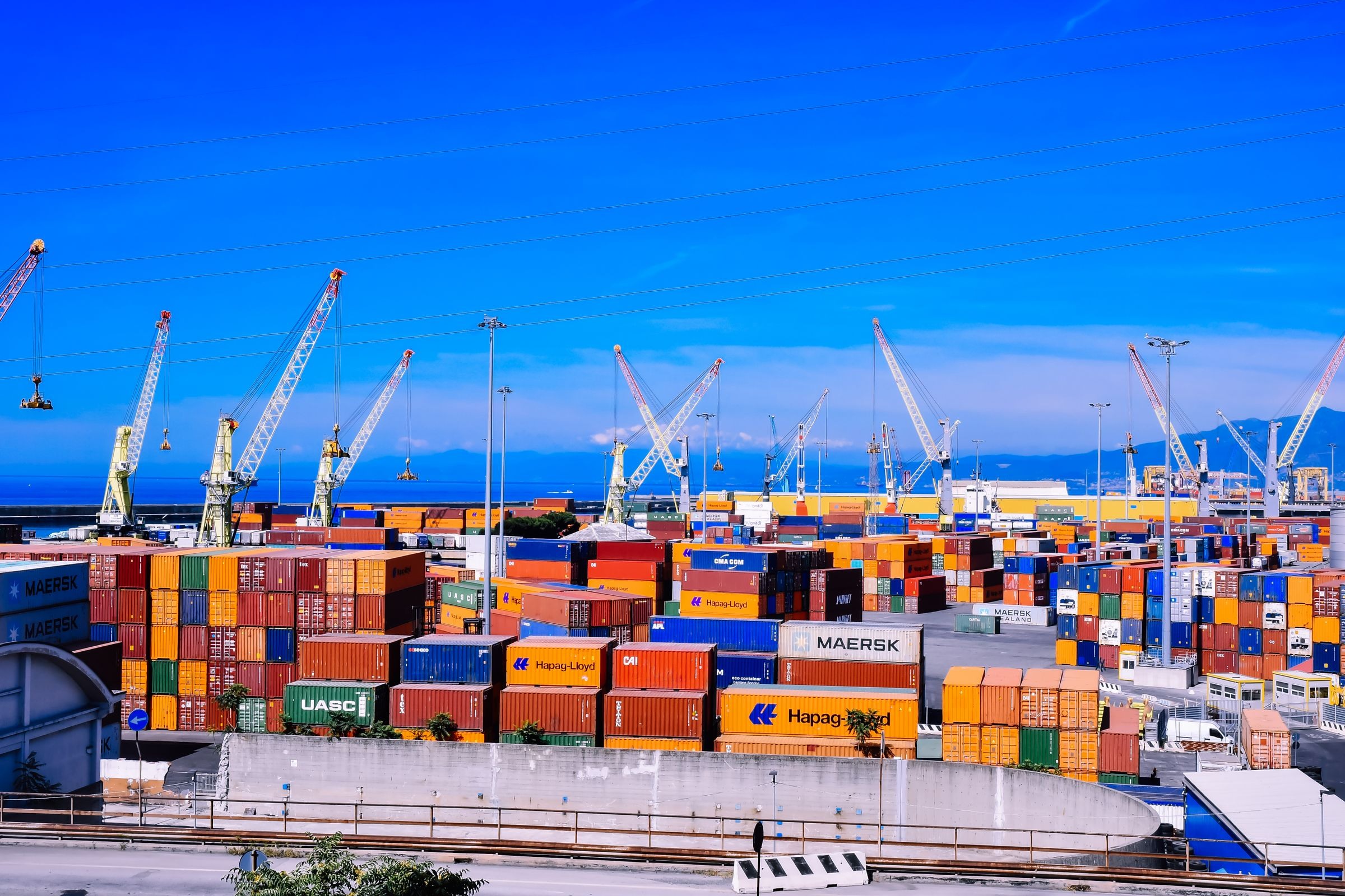 Shipping containers stacked beneath port cranes