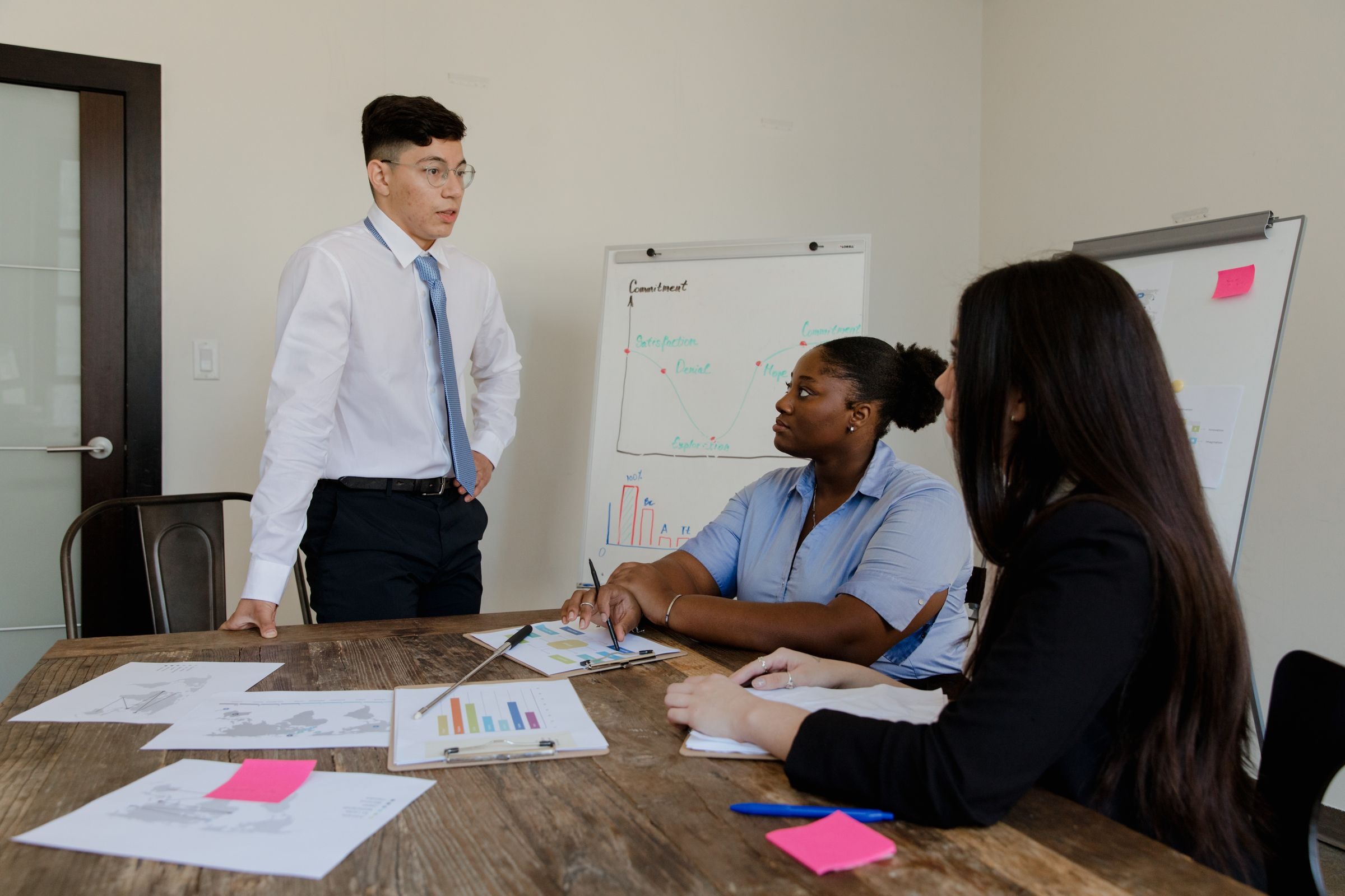 A presenter discussing charts with colleagues in a small meeting room
