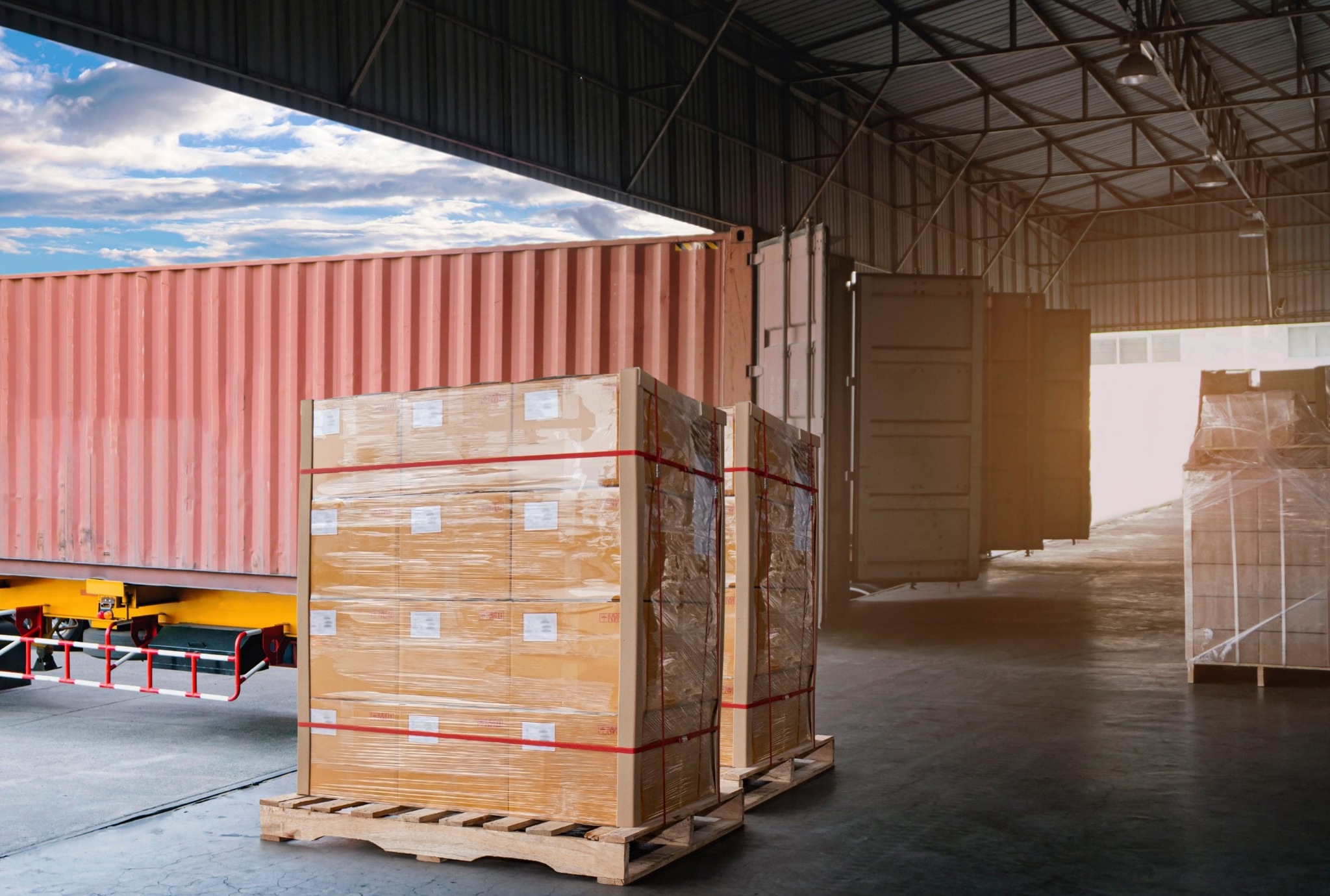 Palletised cartons beside a shipping container in a cargo warehouse