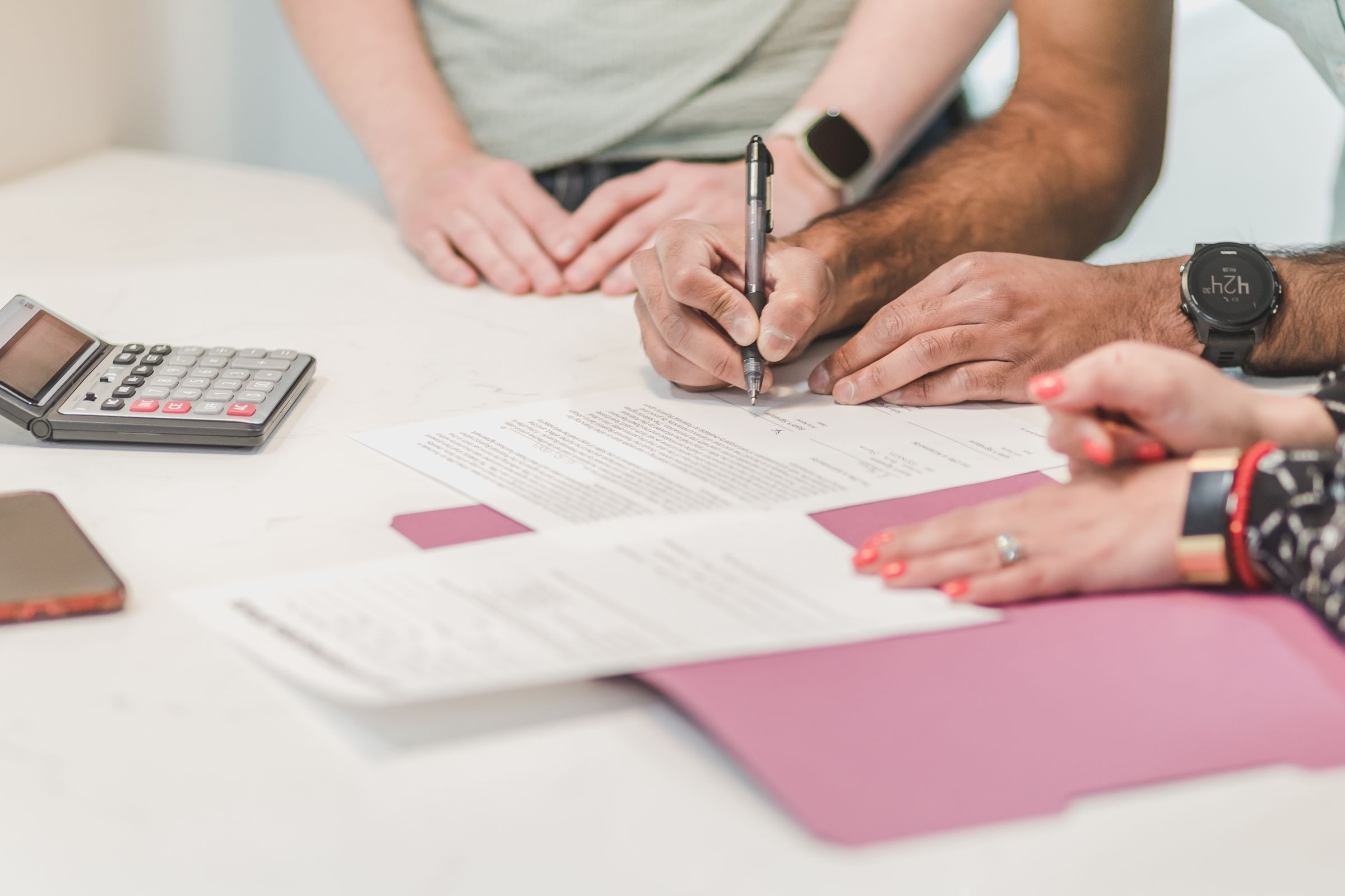 Hands reviewing and completing financial paperwork beside a calculator